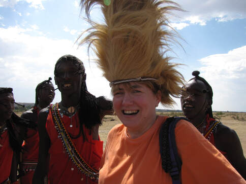 Fotografija: Nasmejana Metka v družbi štirih Masajev. Na glavi nosi pokrivalo iz perja.